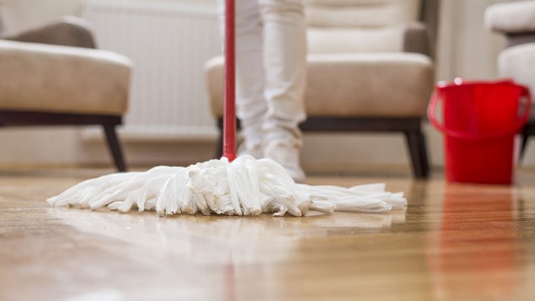 A selective focus shot of a female cleaning the floor with a mop