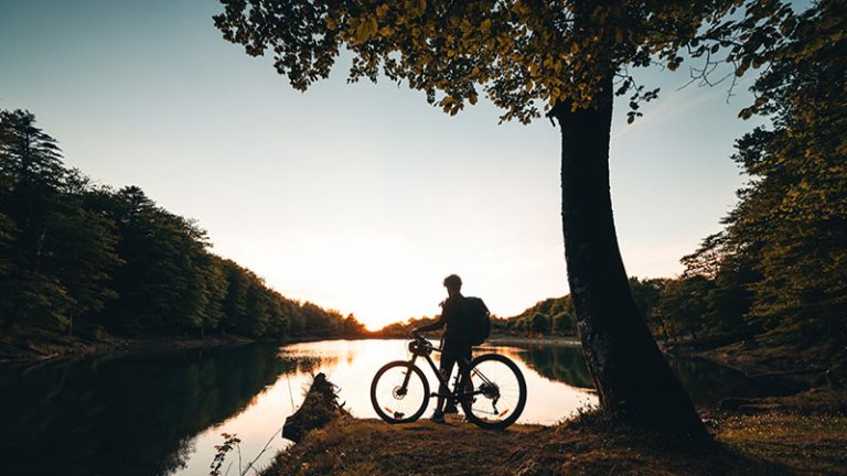 Boy stop by the lake at sunset with bicycle. Mountain biking in the mountains